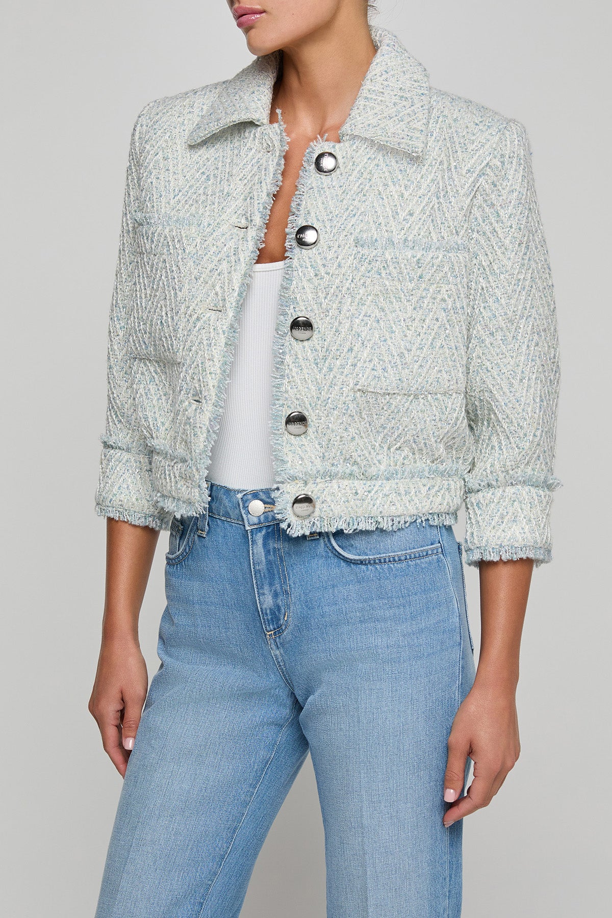 Person wearing a light blue textured jacket and jeans on a gray background