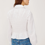 Person wearing a white ribbed sweater over a collared shirt with blue jeans on a light gray background