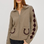 A woman modeling a taupe knit zip-up cardigan with dark brown horseshoe and argyle pattern details, paired with dark jeans against a light gray studio background.