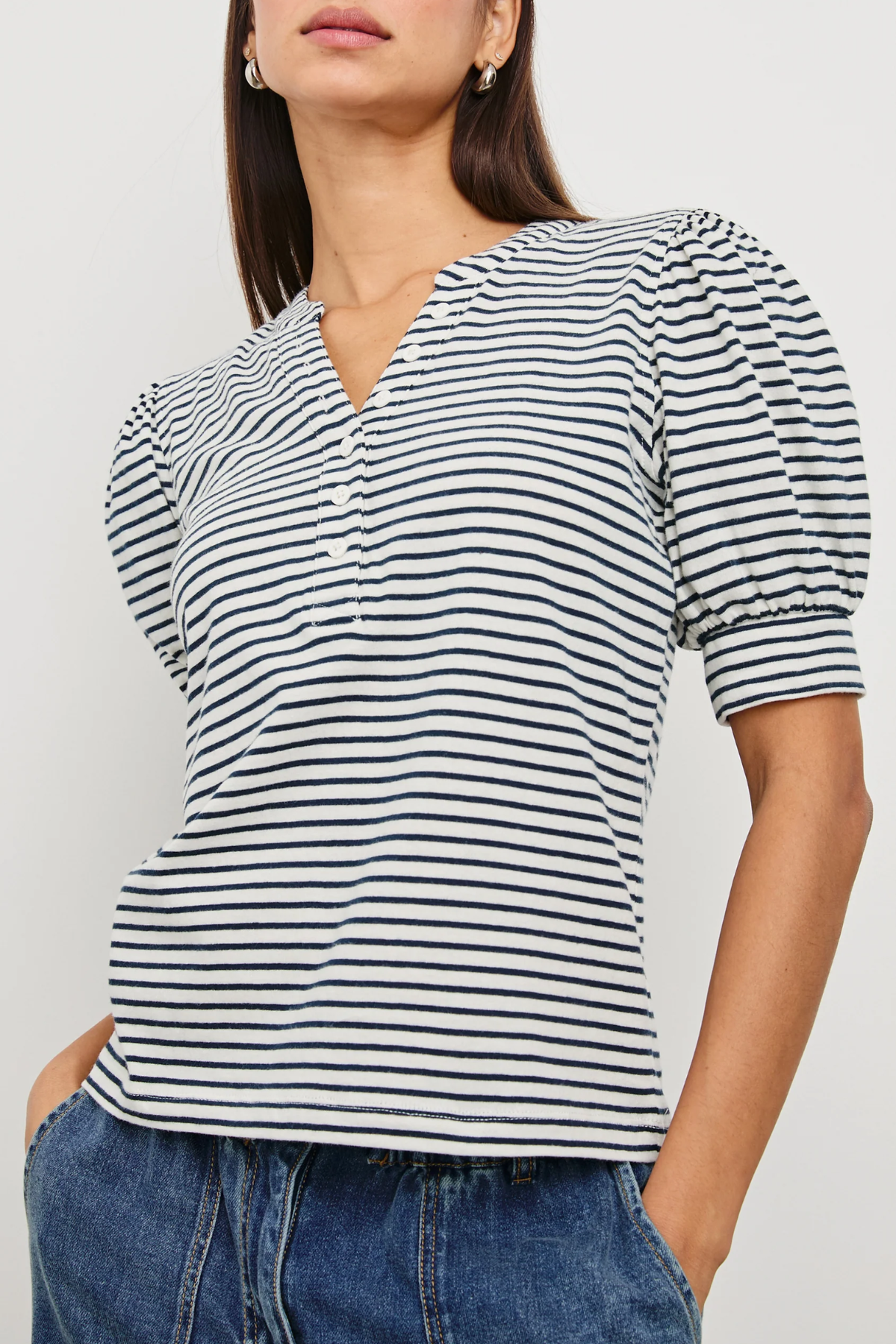 Woman wearing a black and white striped shirt with blue jeans against a plain background