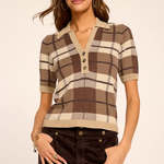 A woman modeling a short-sleeve knit polo-style top with a brown, beige, and cream plaid pattern, paired with dark brown pants, against a plain light beige studio background.
