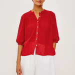 Woman wearing a red blouse and white shorts with a blue and white checkered headscarf on a white background