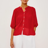 Woman wearing a red blouse and white shorts with a blue and white checkered headscarf on a white background