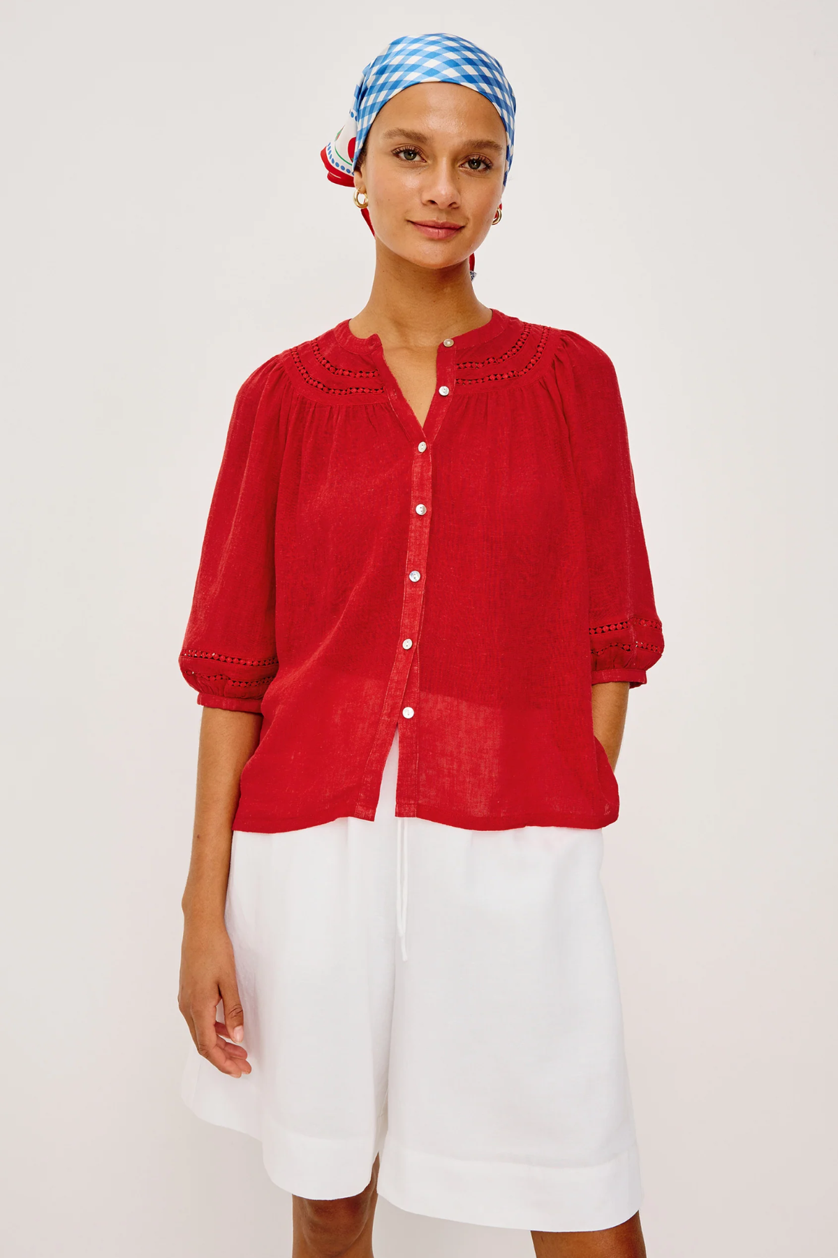 Woman wearing a red blouse and white shorts with a blue and white checkered headscarf on a white background