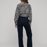 A model shown from the back wearing a long-sleeve button-up shirt with a blue, white, and gray floral pattern, paired with dark navy blue straight-leg jeans and brown shoes, against a light gray studio background.