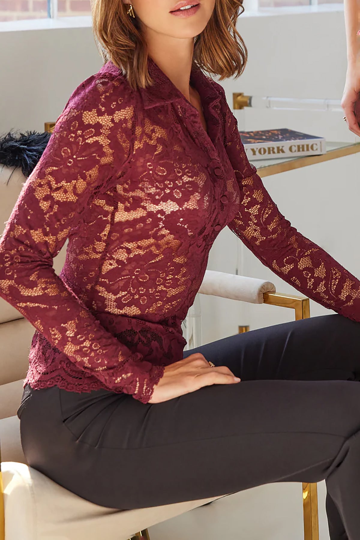 Woman wearing a burgundy lace top sitting on a chair indoors.