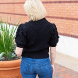 Knit sweater with puff sleeves and pom pom texture, styled with denim.