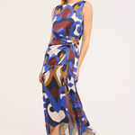 A woman modeling a sleeveless midi dress with an abstract multicolor print in blue, brown, beige, and white, featuring a tie waist and side slit, set against a plain light background.