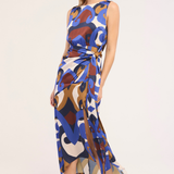 A woman modeling a sleeveless midi dress with an abstract multicolor print in blue, brown, beige, and white, featuring a tie waist and side slit, set against a plain light background.
