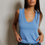 Woman wearing a blue tank top and jeans against a plain background