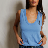 Woman wearing a blue tank top and jeans against a plain background
