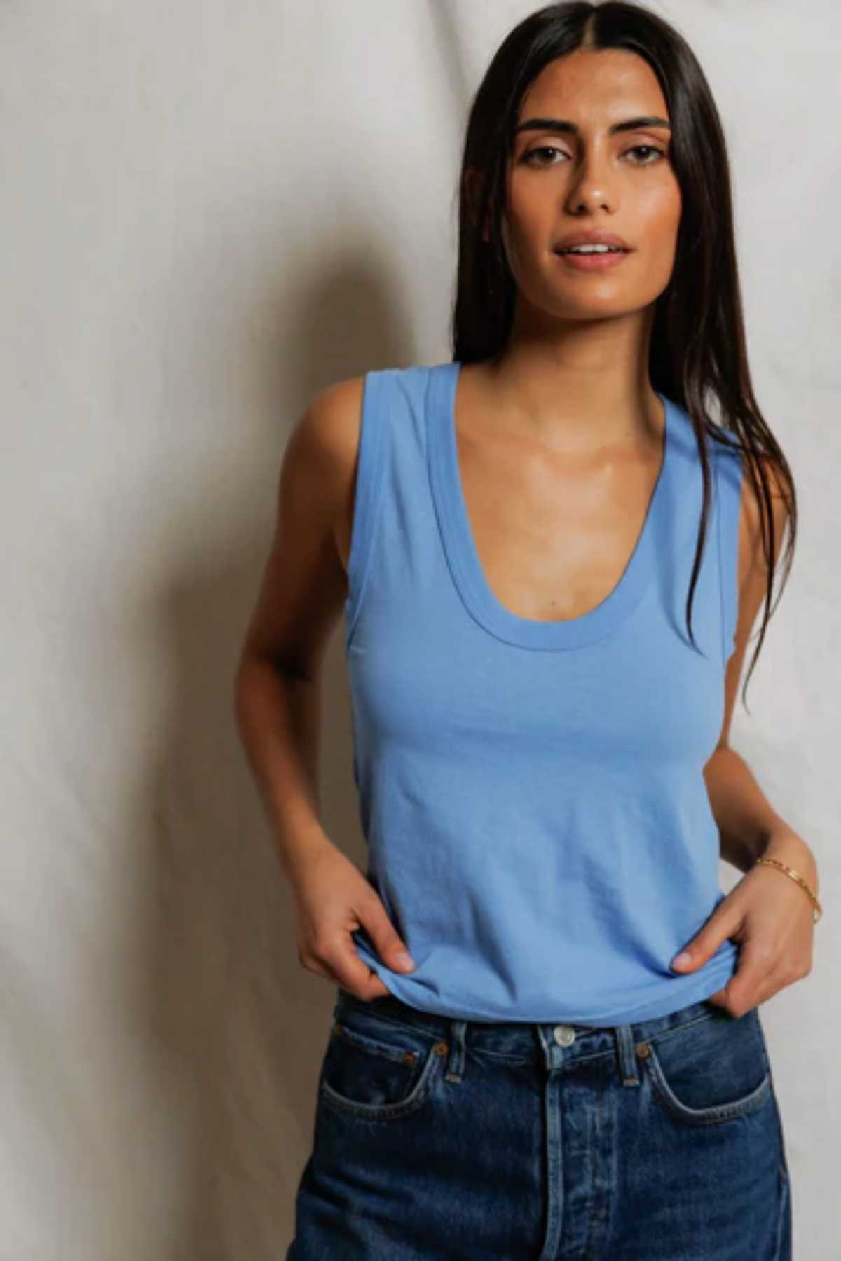 Woman wearing a blue tank top and jeans against a plain background