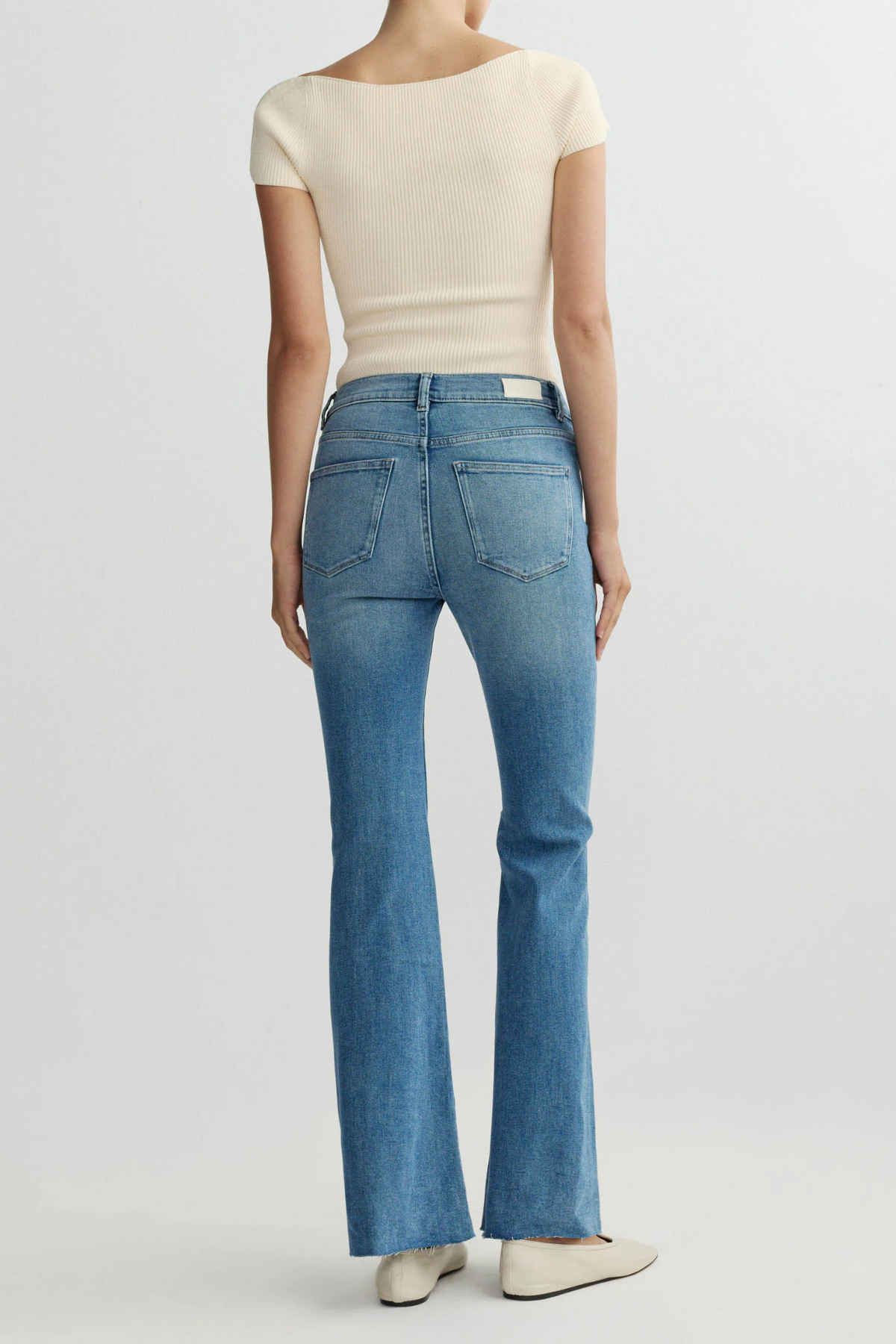 Person wearing a cream top and blue jeans on a white background