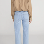 Person wearing a beige blouse and light blue jeans on a plain background
