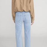 Person wearing a beige blouse and light blue jeans on a plain background
