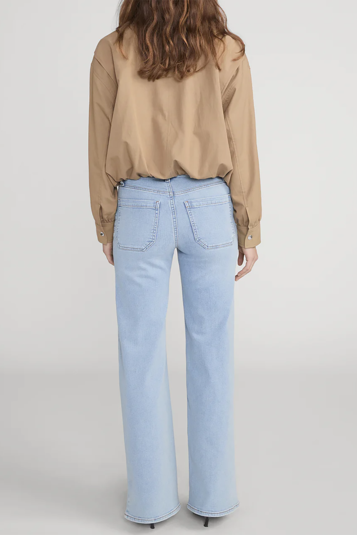 Person wearing a beige blouse and light blue jeans on a plain background