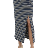 A navy blue midi skirt with thin cream and white horizontal stripes, featuring a front button closure and a high side slit, shown on a model wearing metallic sandals against a white background.