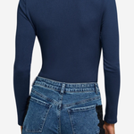 A woman shown from the back wearing a navy blue long-sleeve top with lace detailing at the neckline and blue jeans with black lace side panels, against a light gray studio background.