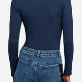 A woman shown from the back wearing a navy blue long-sleeve top with lace detailing at the neckline and blue jeans with black lace side panels, against a light gray studio background.