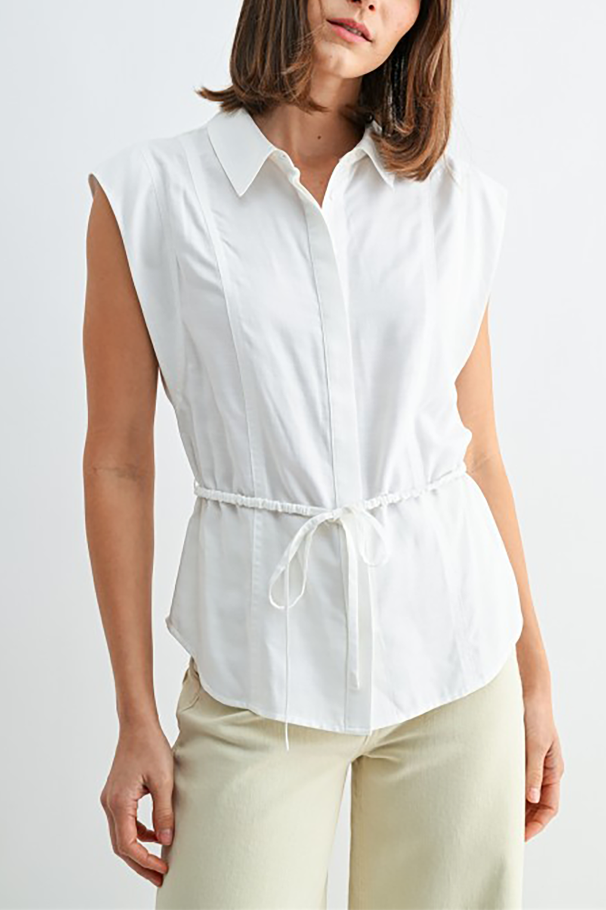 Woman wearing a white sleeveless blouse with a tie waist on a plain background