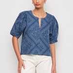 Woman wearing a blue patterned top and white shorts on a light background