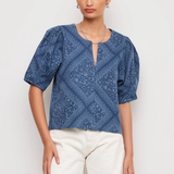 Woman wearing a blue patterned top and white shorts on a light background