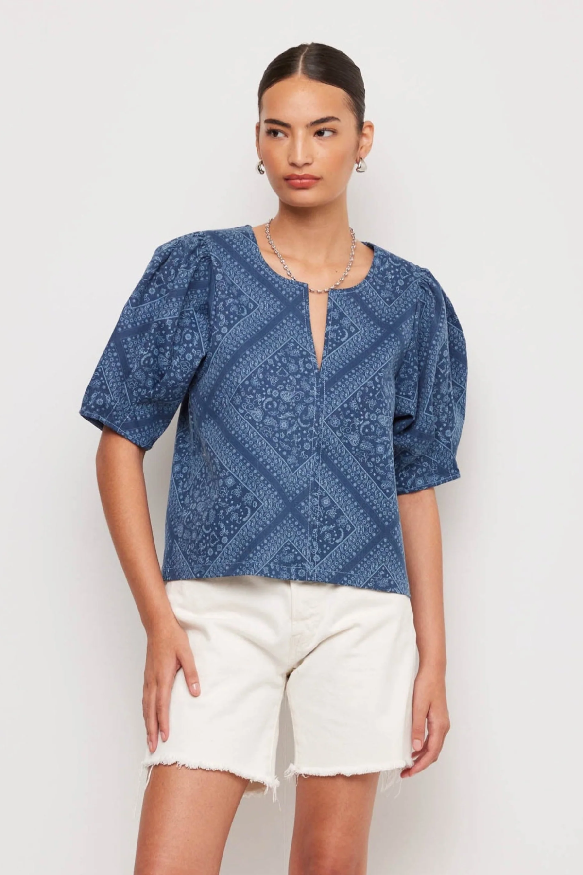 Woman wearing a blue patterned top and white shorts on a light background