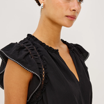Woman wearing a black top with ruffled details on a plain background