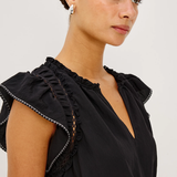 Woman wearing a black top with ruffled details on a plain background