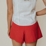 Person wearing a white sleeveless top and red shorts on a beige background