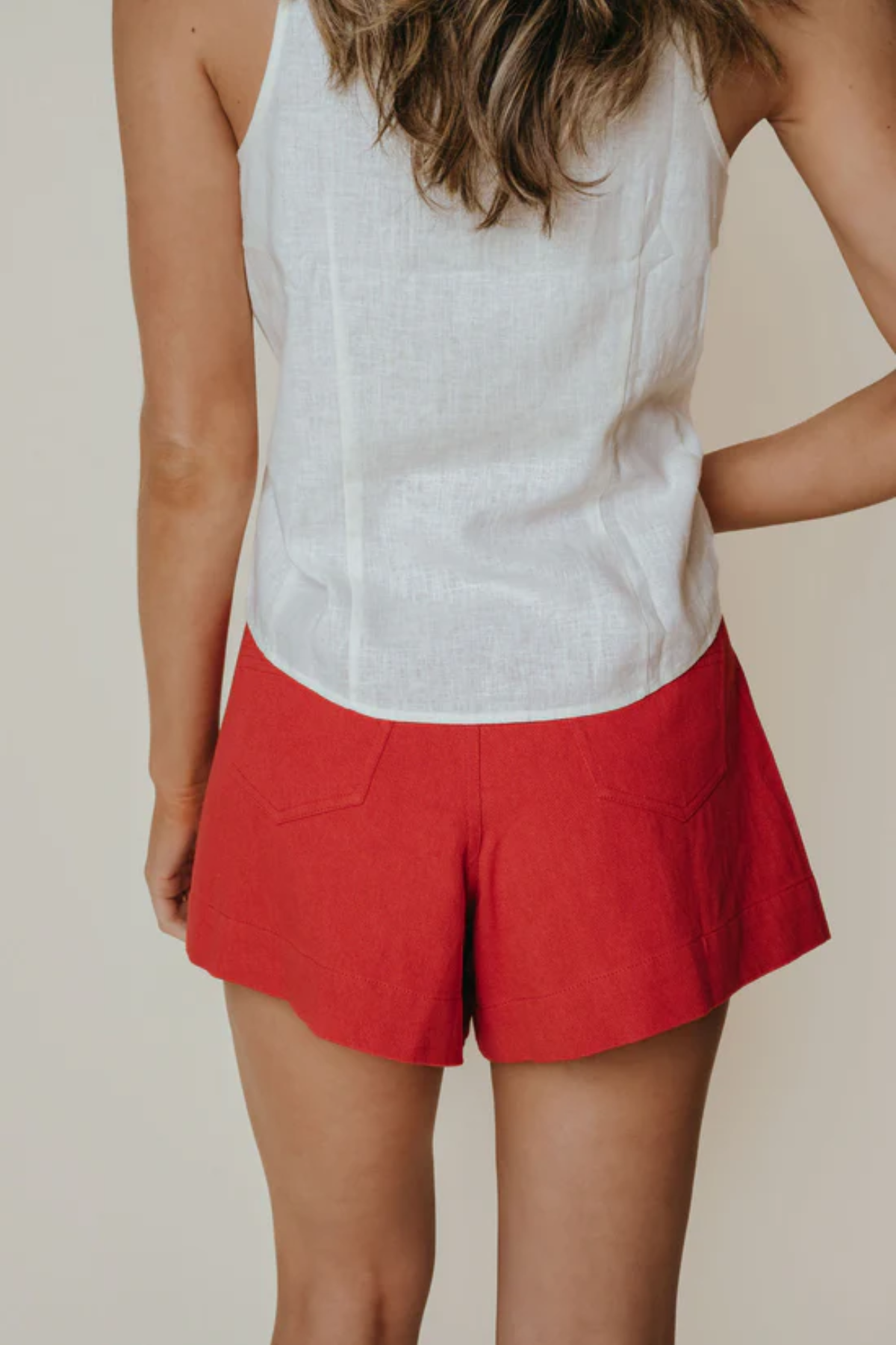 Person wearing a white sleeveless top and red shorts on a beige background