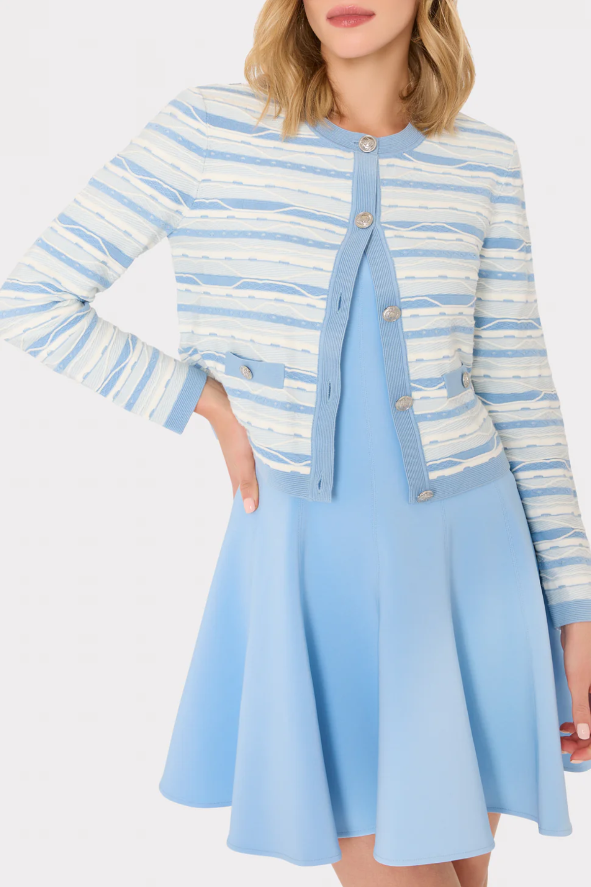Woman wearing a blue and white striped cardigan over a light blue dress on a white background