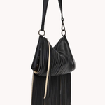 A black pleated leather shoulder bag with a long strap, a slouchy crescent shape, and a long fringe detail hanging from the bottom, shown against a plain off-white background.