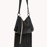 A black pleated leather shoulder bag with a long strap, a slouchy crescent shape, and a long fringe detail hanging from the bottom, shown against a plain off-white background.