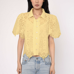 Woman wearing a yellow lace blouse and light blue jeans against a white background