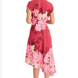 Model wearing a vibrant pink printed short-sleeve midi dress with an asymmetrical hem and flowing silhouette.
