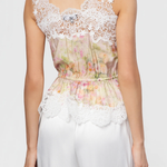 Woman wearing a floral top with lace details and white pants on a plain background