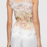 Woman wearing a floral top with lace details and white pants on a plain background