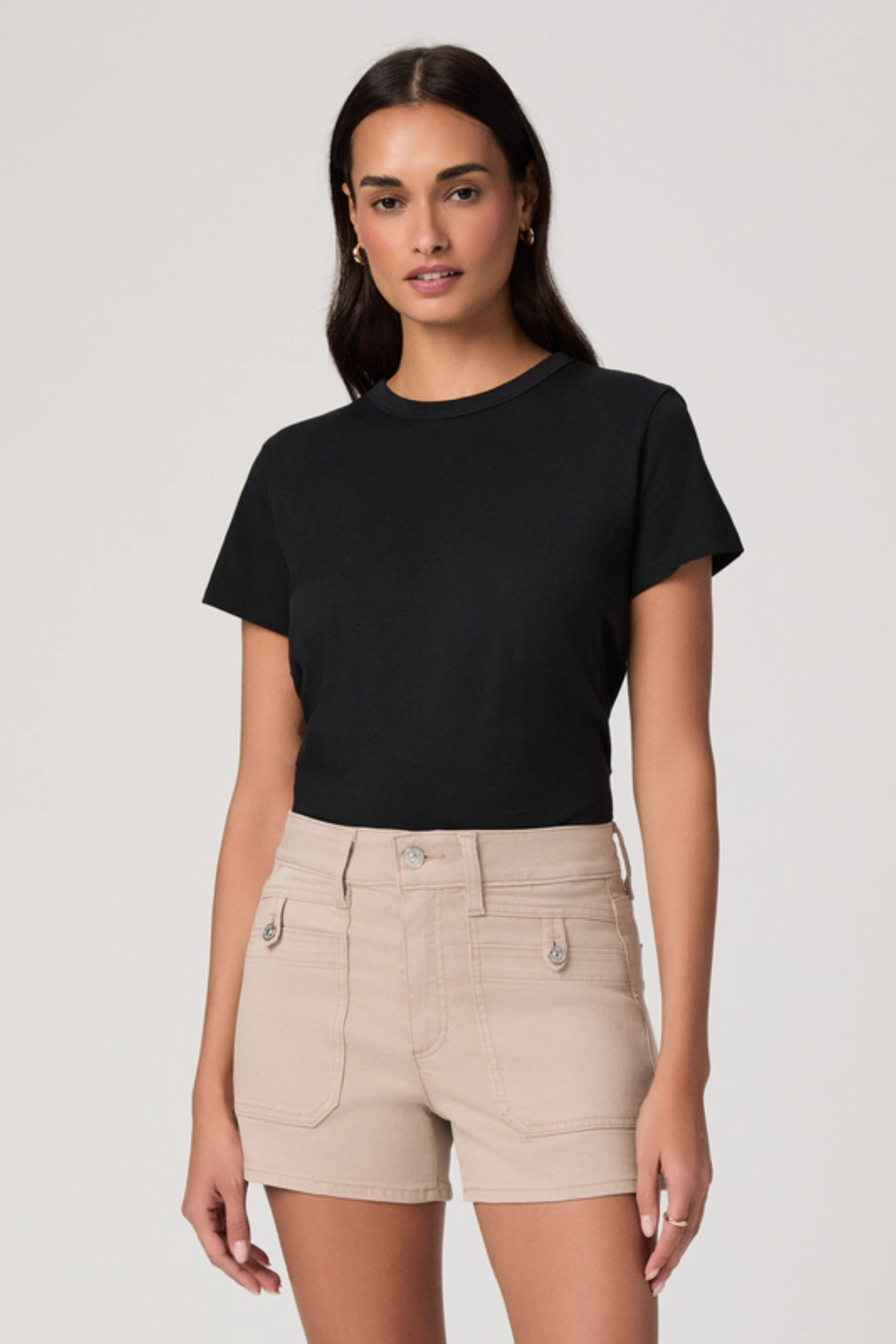 Woman wearing a black t-shirt and beige shorts on a plain background