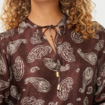 A close-up of a woman wearing a brown long-sleeve blouse with a white paisley pattern and a keyhole tie neckline.