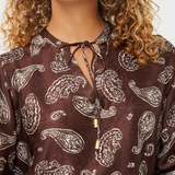 A close-up of a woman wearing a brown long-sleeve blouse with a white paisley pattern and a keyhole tie neckline.