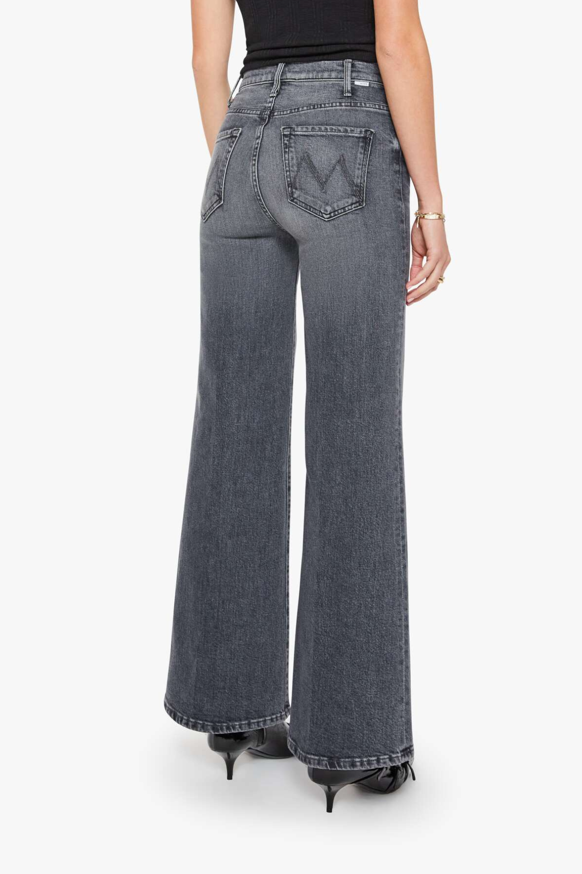 A model shown from the back wearing a pair of wide-leg, high-waisted gray denim jeans with a distinctive 'W' logo on the back pocket, paired with a black top and black heels against a plain white background.