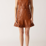 A woman modeling a sleeveless brown faux-leather mini dress with a V-neck, matching belt, and floral embroidery on the bodice and flared hem, paired with brown strappy heeled sandals against a light beige studio background.