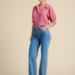 Woman wearing a pink shirt and blue jeans against a beige background
