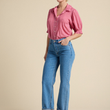 Woman wearing a pink shirt and blue jeans against a beige background