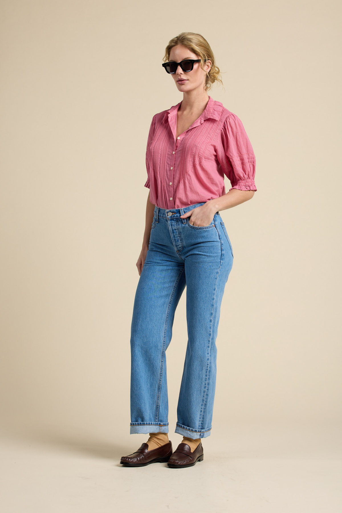 Woman wearing a pink shirt and blue jeans against a beige background