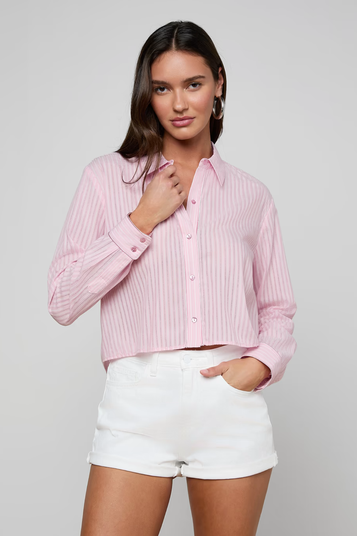 Woman wearing a pink ribbed blouse and white shorts on a gray background