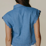Blue denim vest with scalloped edges worn by a person on a beige background