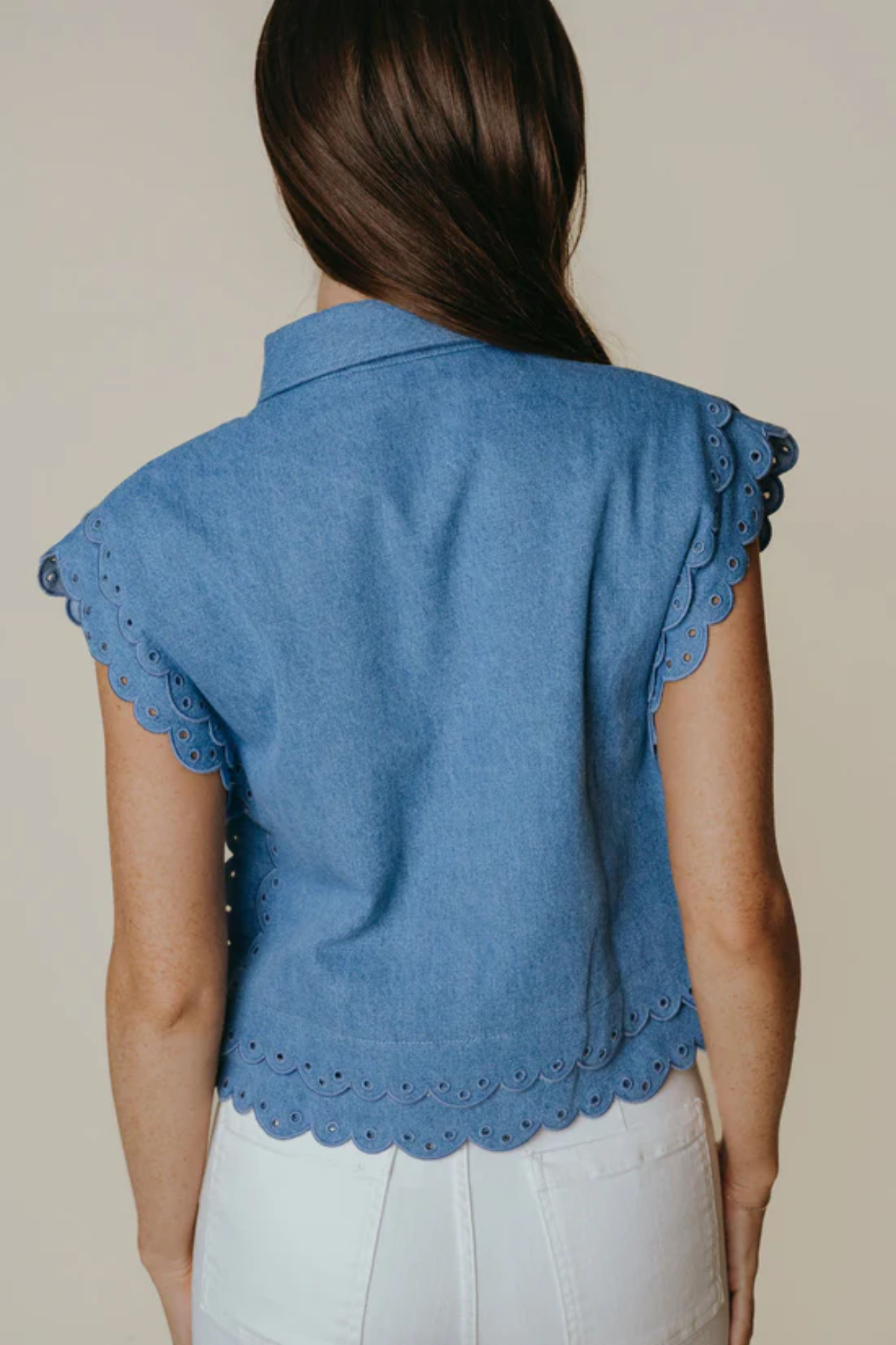 Blue denim vest with scalloped edges worn by a person on a beige background