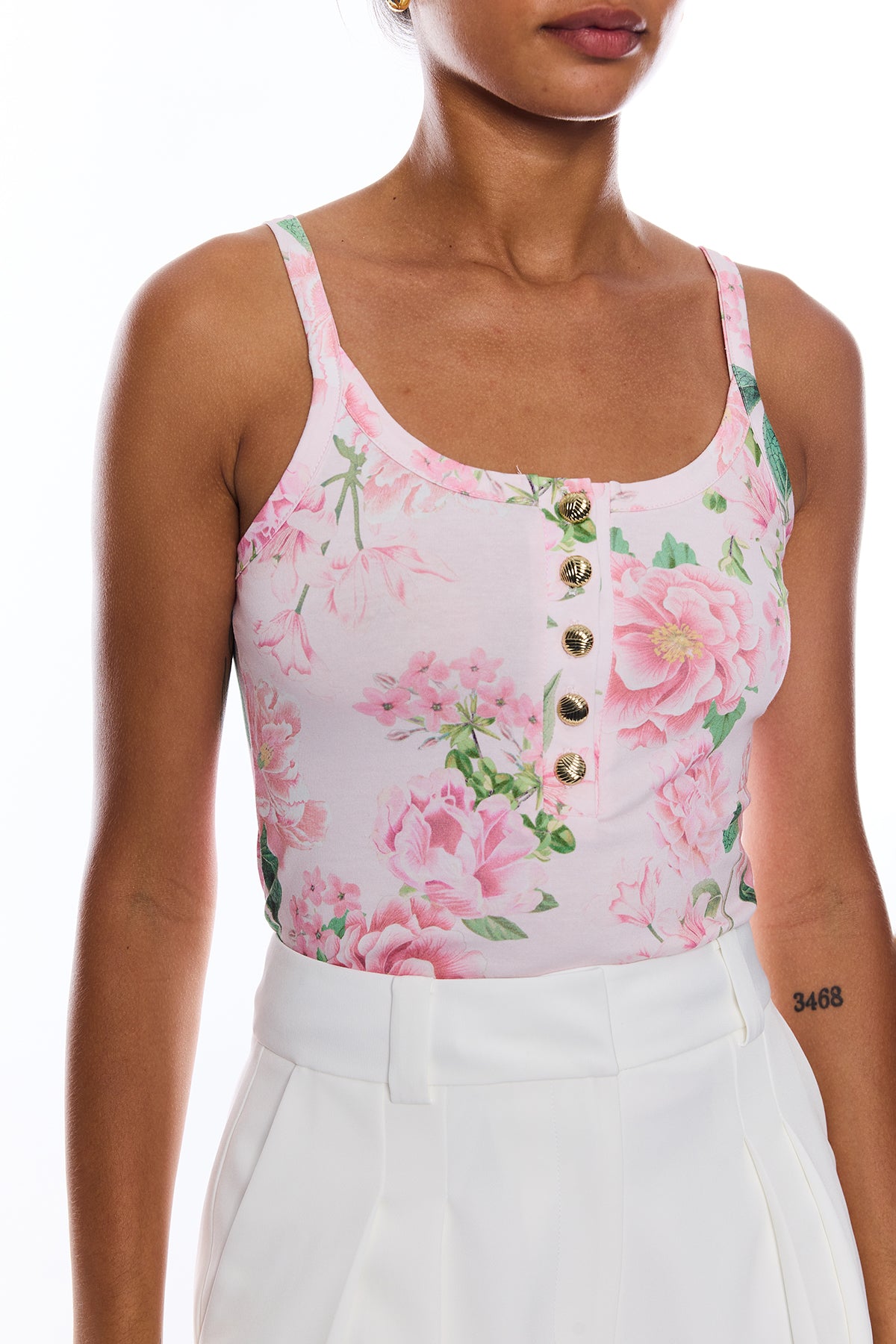 Woman wearing a floral tank top with white pants on a white background